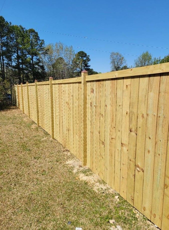 Wooden privacy fence along a grassy yard under a clear blue sky.