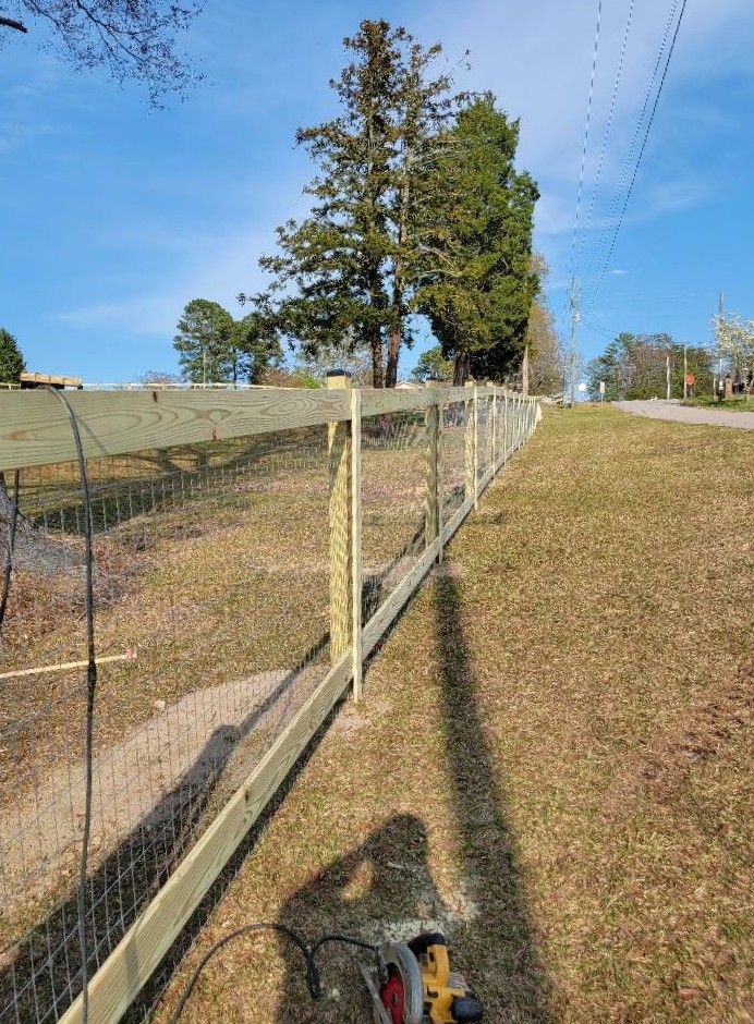 Fence along a grassy slope beside a dirt path under a clear blue sky.