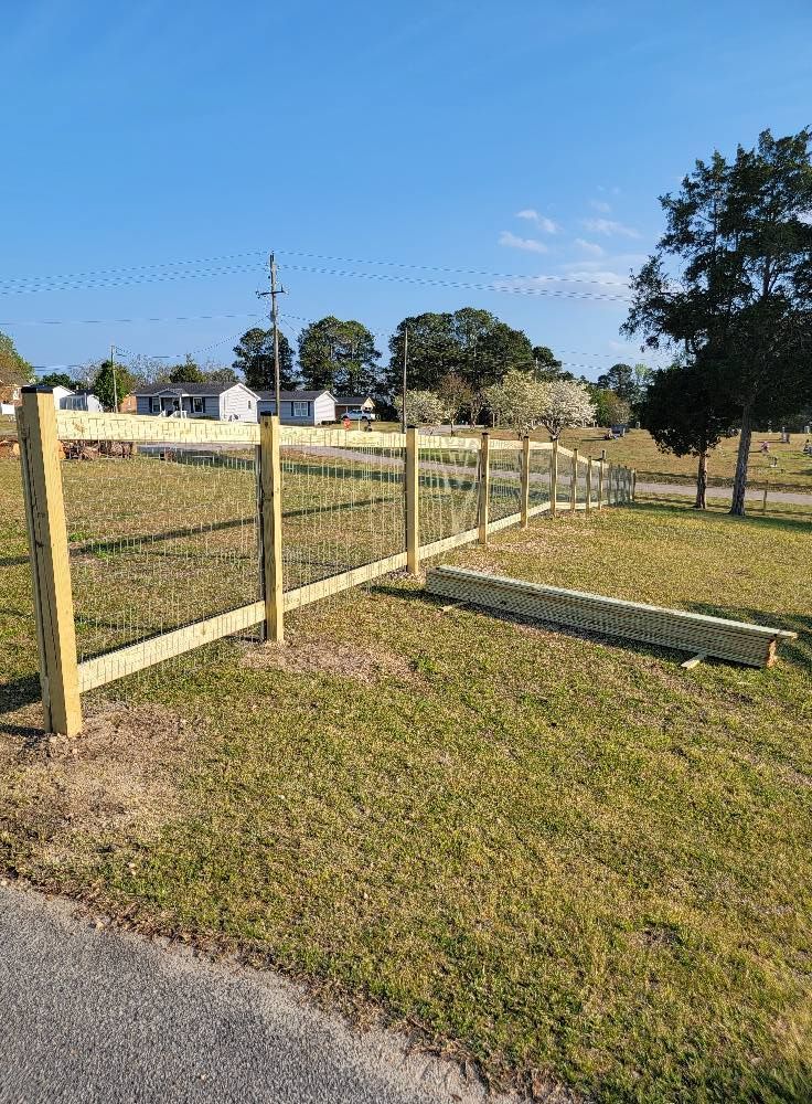 Wooden split-rail fence along a grassy roadside under a clear blue sky