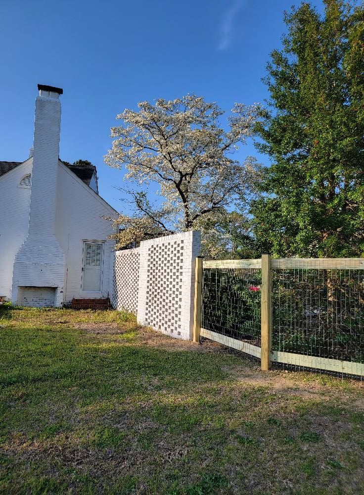 White house with chimney beside a wooden fence and gate under a blue sky.