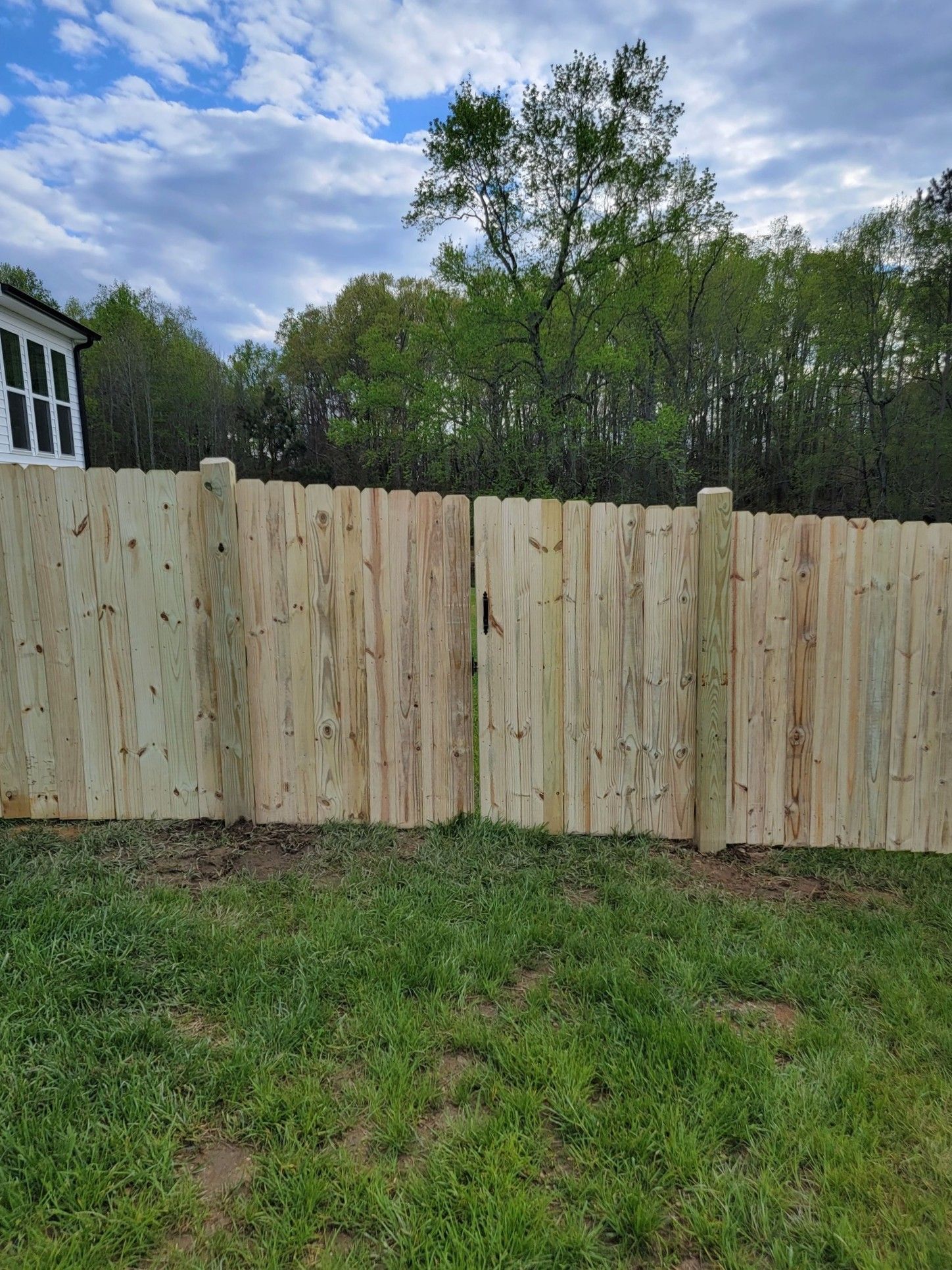 New wooden fence in a grassy yard under a partly cloudy sky