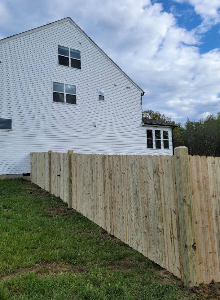White two-story house behind a wooden fence under a partly cloudy sky.