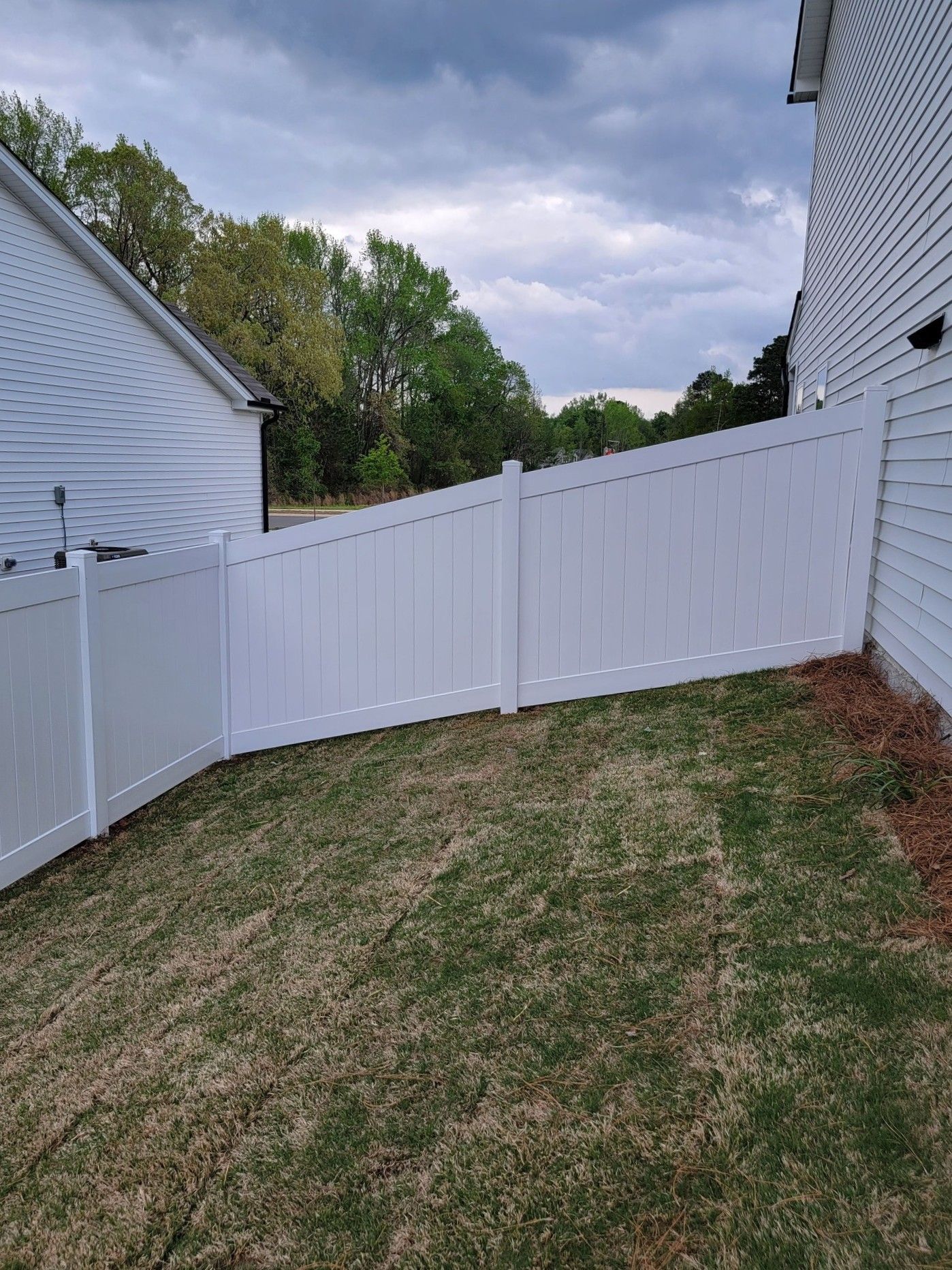 White vinyl fence gate in a sloped backyard between two houses under a cloudy sky
