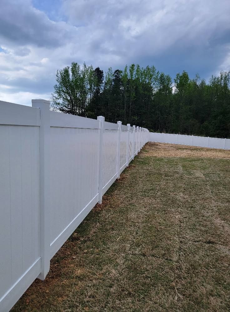 White vinyl fence along a grassy yard under a cloudy sky with trees in the background