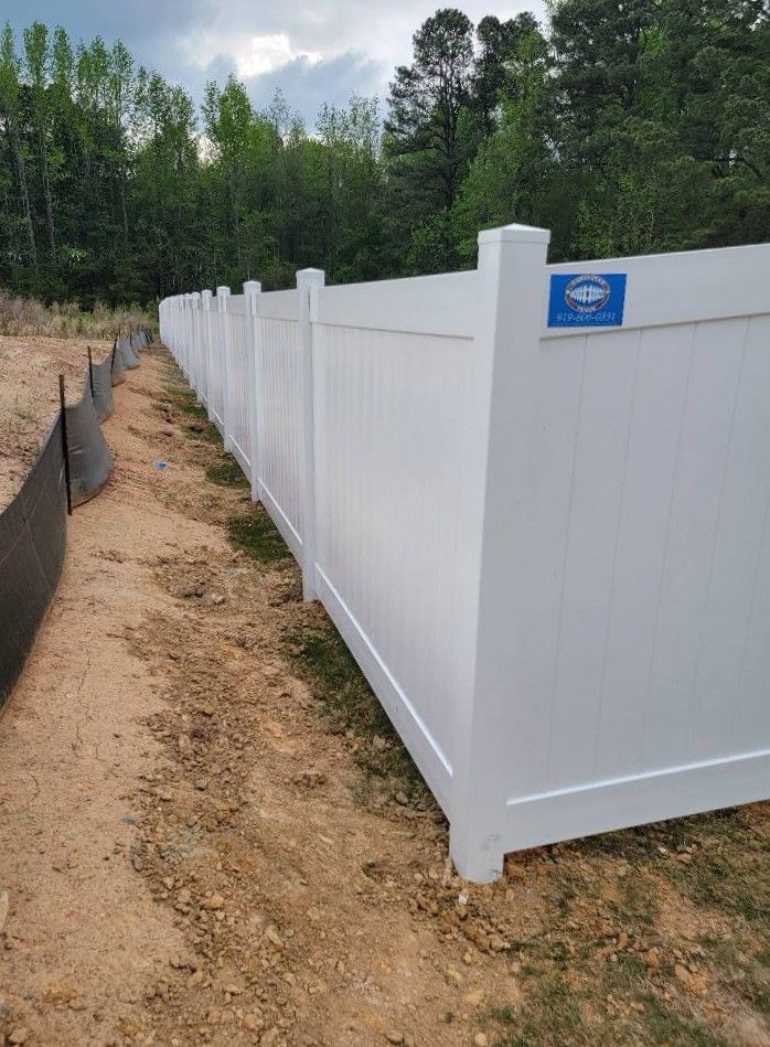 White vinyl fence lining a dirt path beside a wooded area