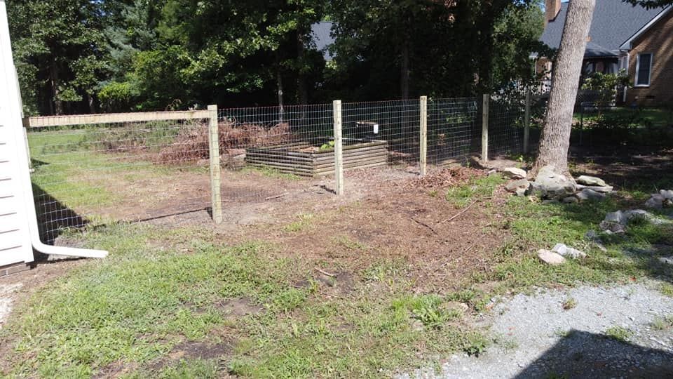Backyard with a wire fence, dirt patch, grass, trees, and a house in the background