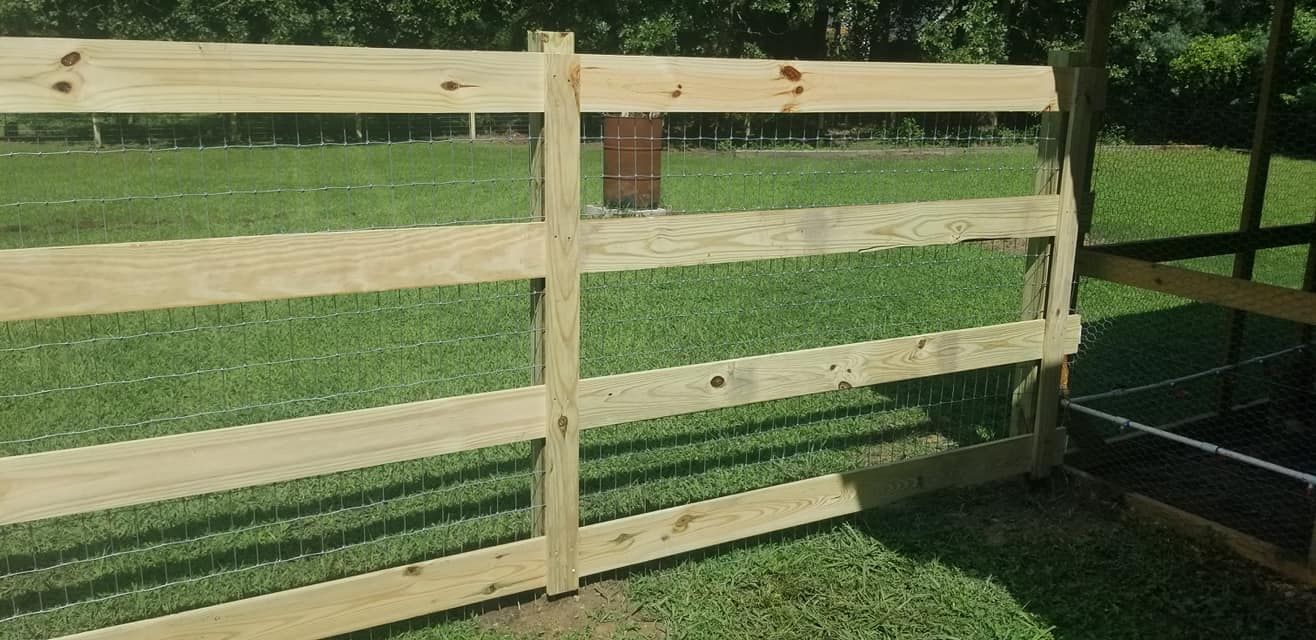 Wooden fence on a grassy field with a dark metal gate on the right