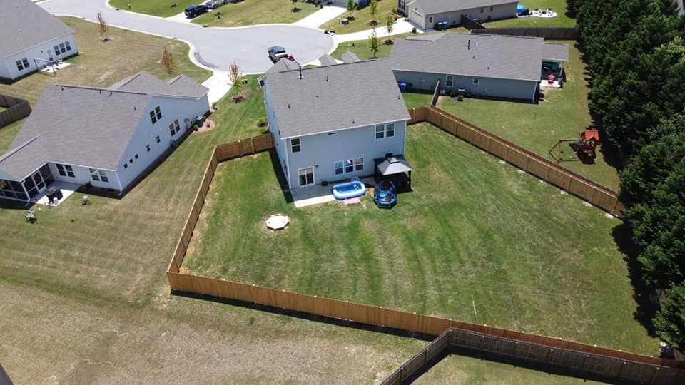Aerial view of suburban houses with fenced backyards and parked cars on a sunny day