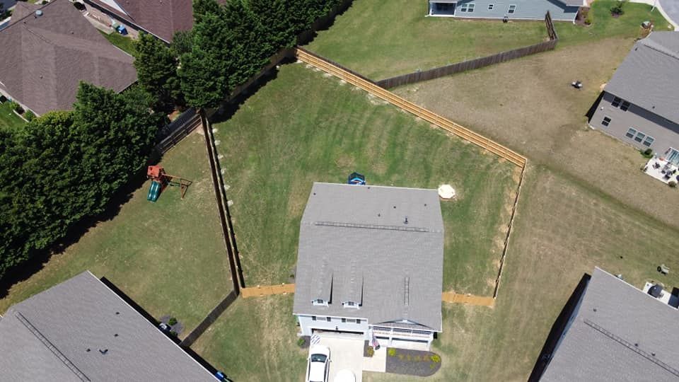 Aerial view of a backyard with a gray-roofed house, green lawn, trees, and neighboring homes.