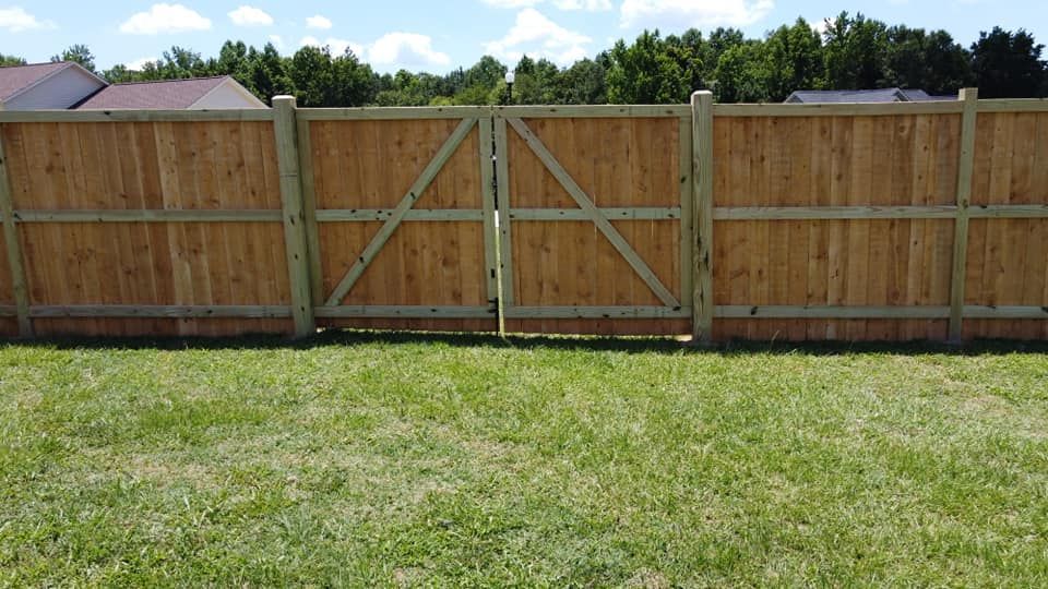 Wooden privacy fence with a double gate behind a grassy lawn under a partly cloudy sky
