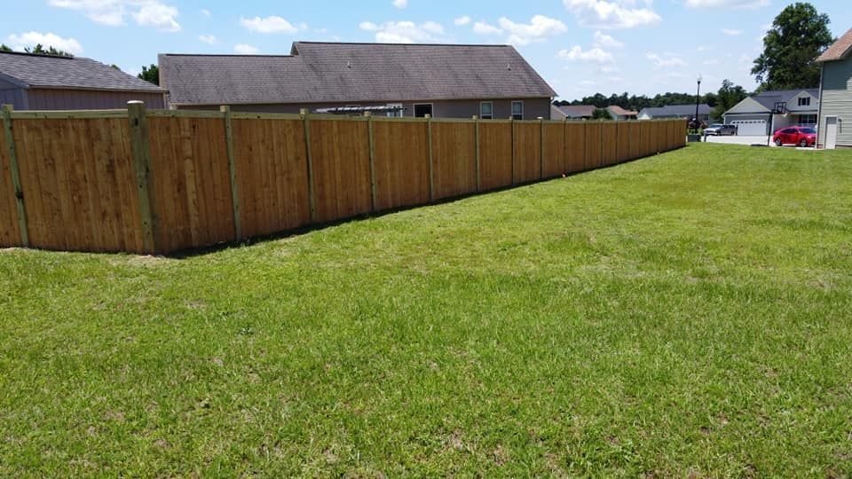 Grassy vacant lot beside a long wooden fence and houses under a blue sky
