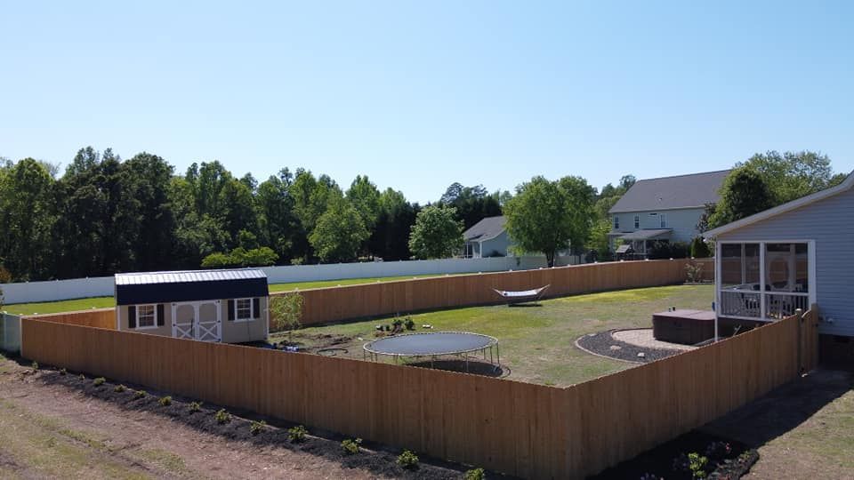 Backyard fenced yard with a small shed, raised garden beds, and a house under a clear blue sky