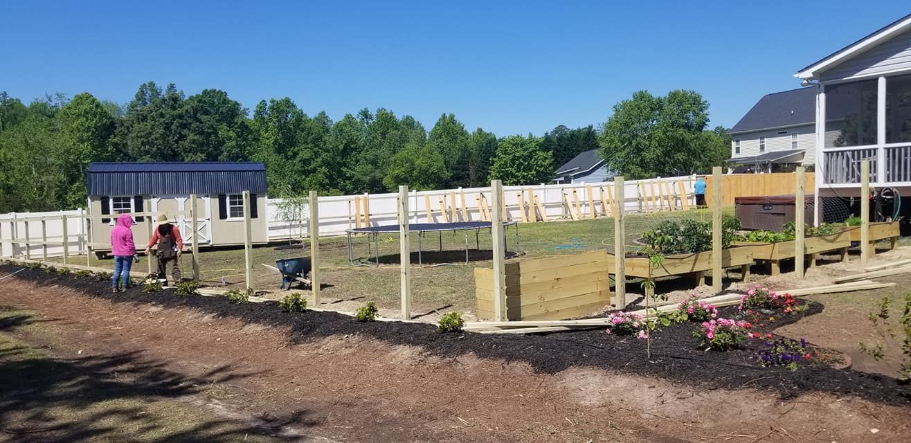 Sunny fenced garden with wooden posts, two people, and a blue-roofed shed under a clear sky