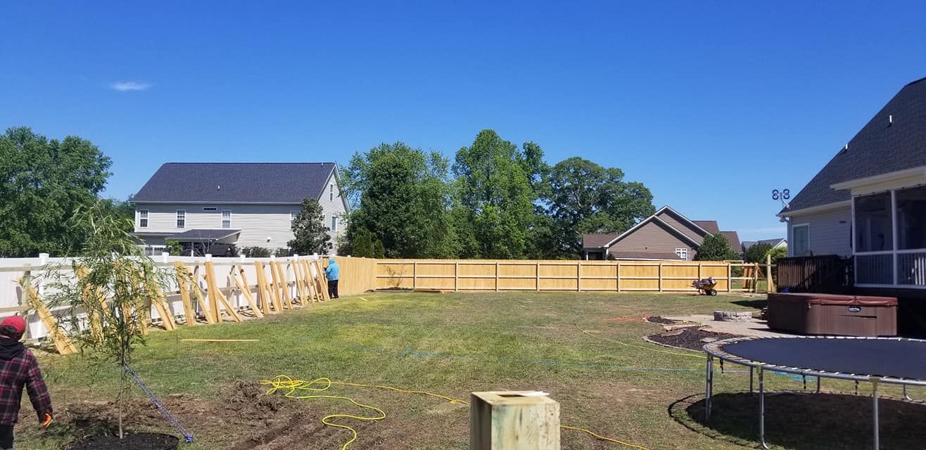 Backyard with a wooden fence, grassy yard, houses, and a person working near stacked boards