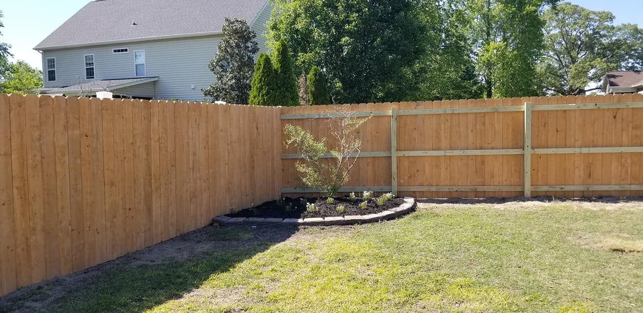 Backyard with a wooden fence, raised garden bed, and grassy lawn in sunlight