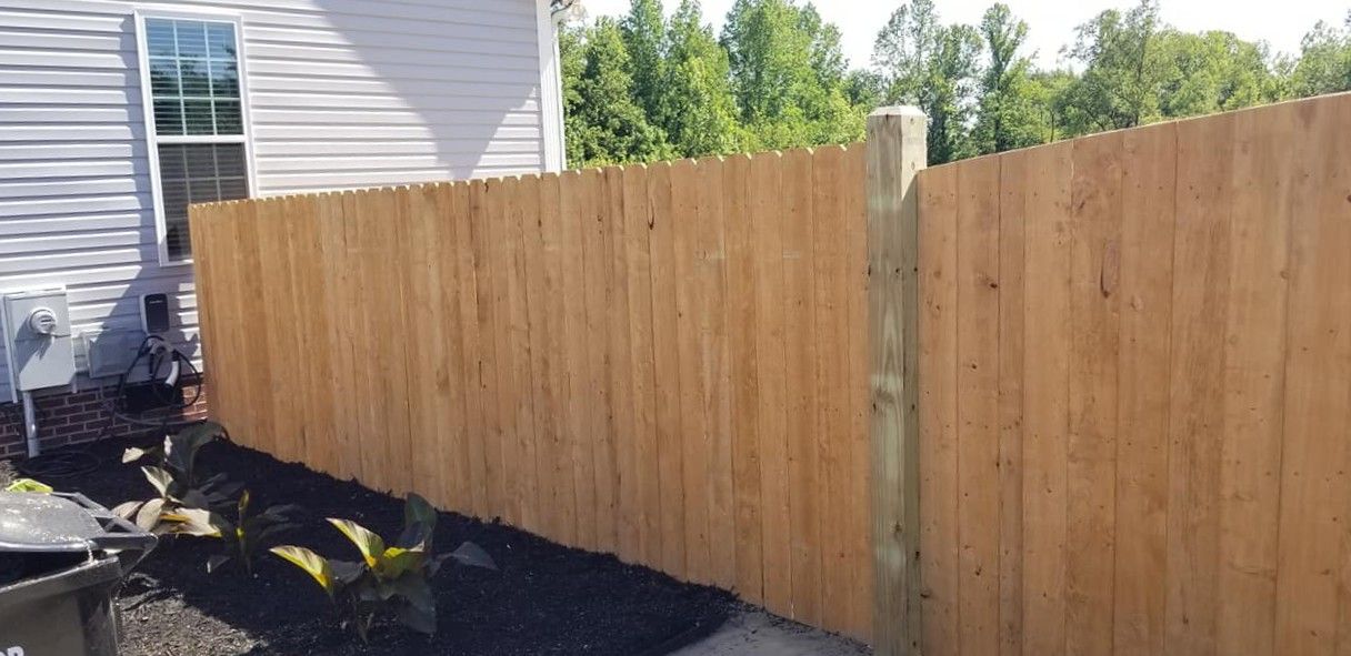 Wooden privacy fence beside a gray house, with black landscape fabric along the base.