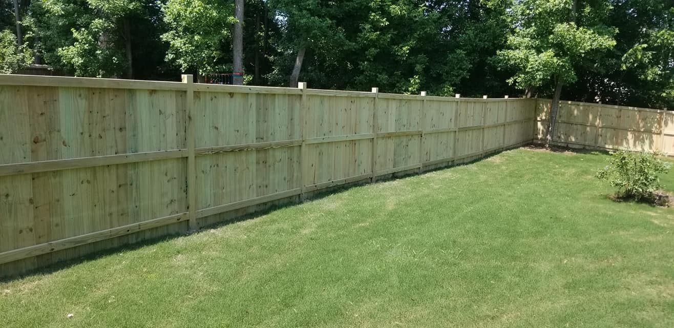 Wooden privacy fence along a green backyard lawn beside trees and shrubs