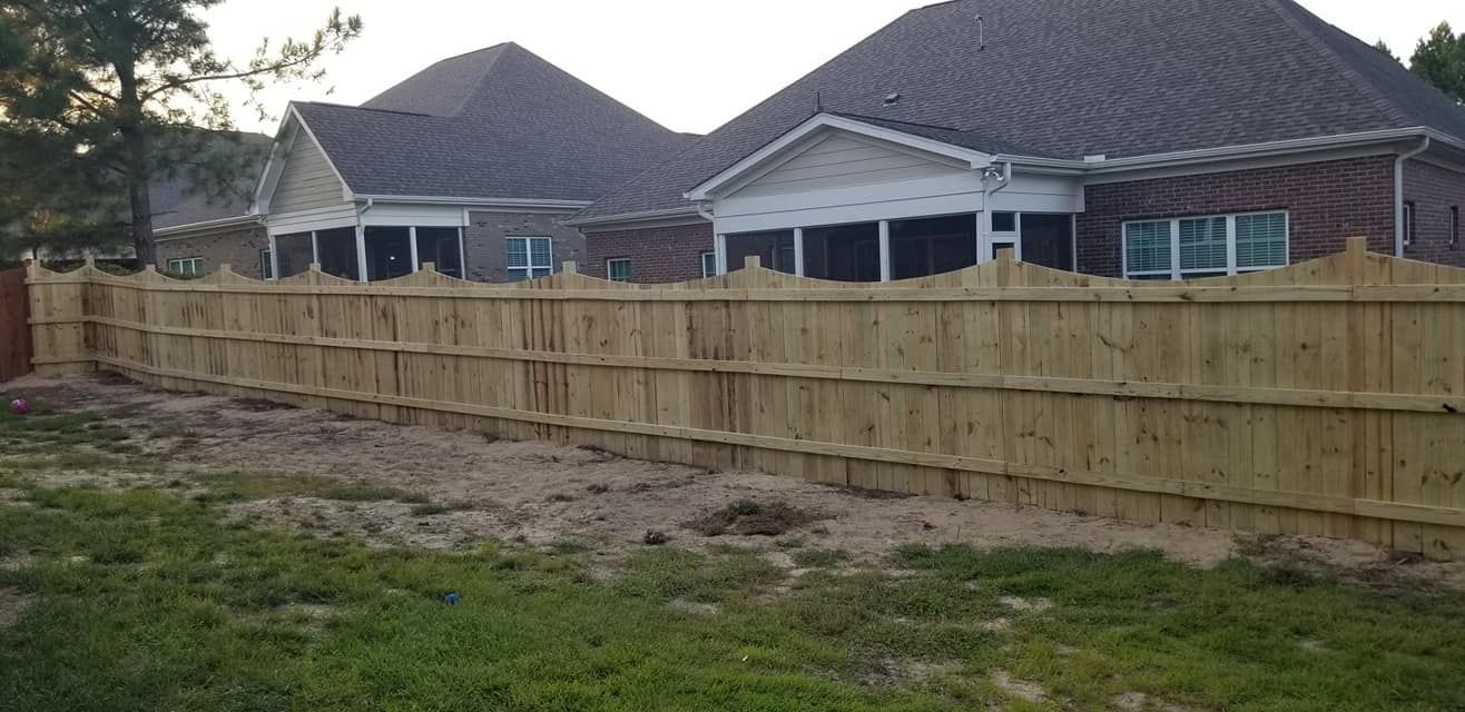 Wooden privacy fence along a grassy yard with brick houses in the background.
