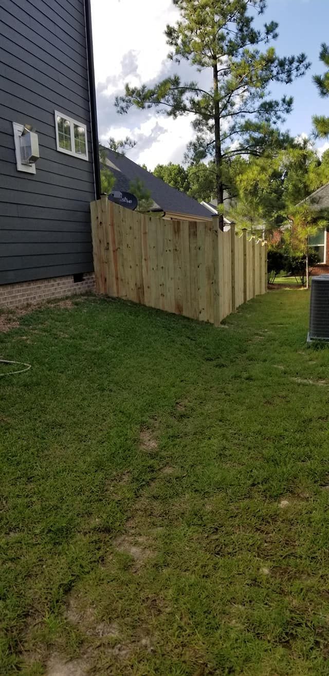 Wooden fence panel beside a dark house in a grassy yard, with trees and a cloudy sky.