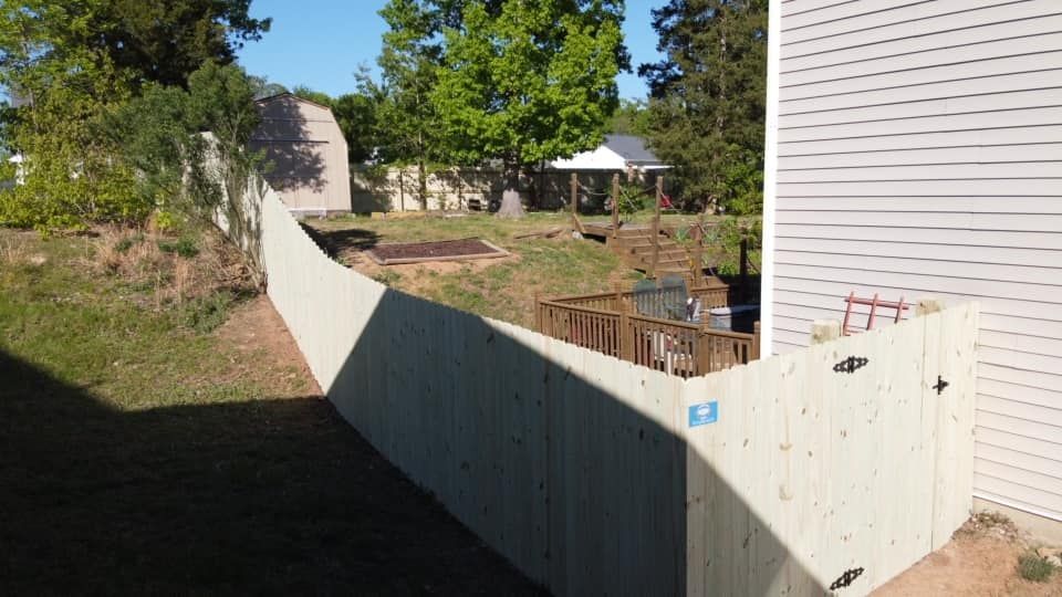 Backyard with a white fence, grassy slope, deck, and house in sunlight