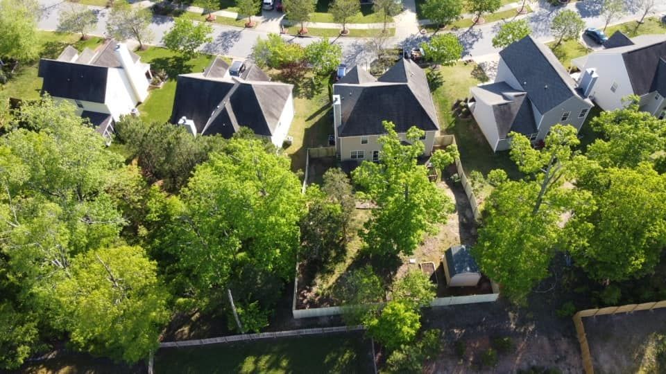 Aerial view of homes with gray roofs surrounded by dense green trees and a central walkway