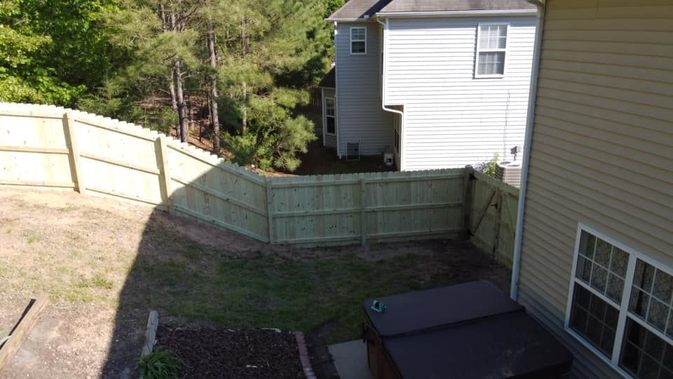 Backyard with a wooden fence, grass, trees, and the side of a house in sunlight