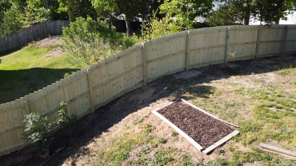 Curved wooden fence in a sunny backyard beside a raised garden bed and grassy slope
