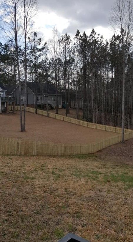 Backyard with a fenced dirt area, sparse trees, and a house under a cloudy sky