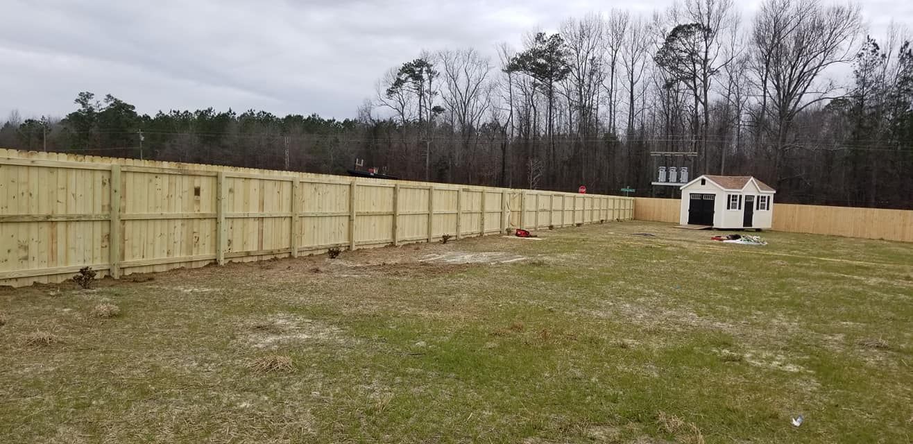 Wide grassy yard with a long wooden fence and a small white shed under cloudy skies.
