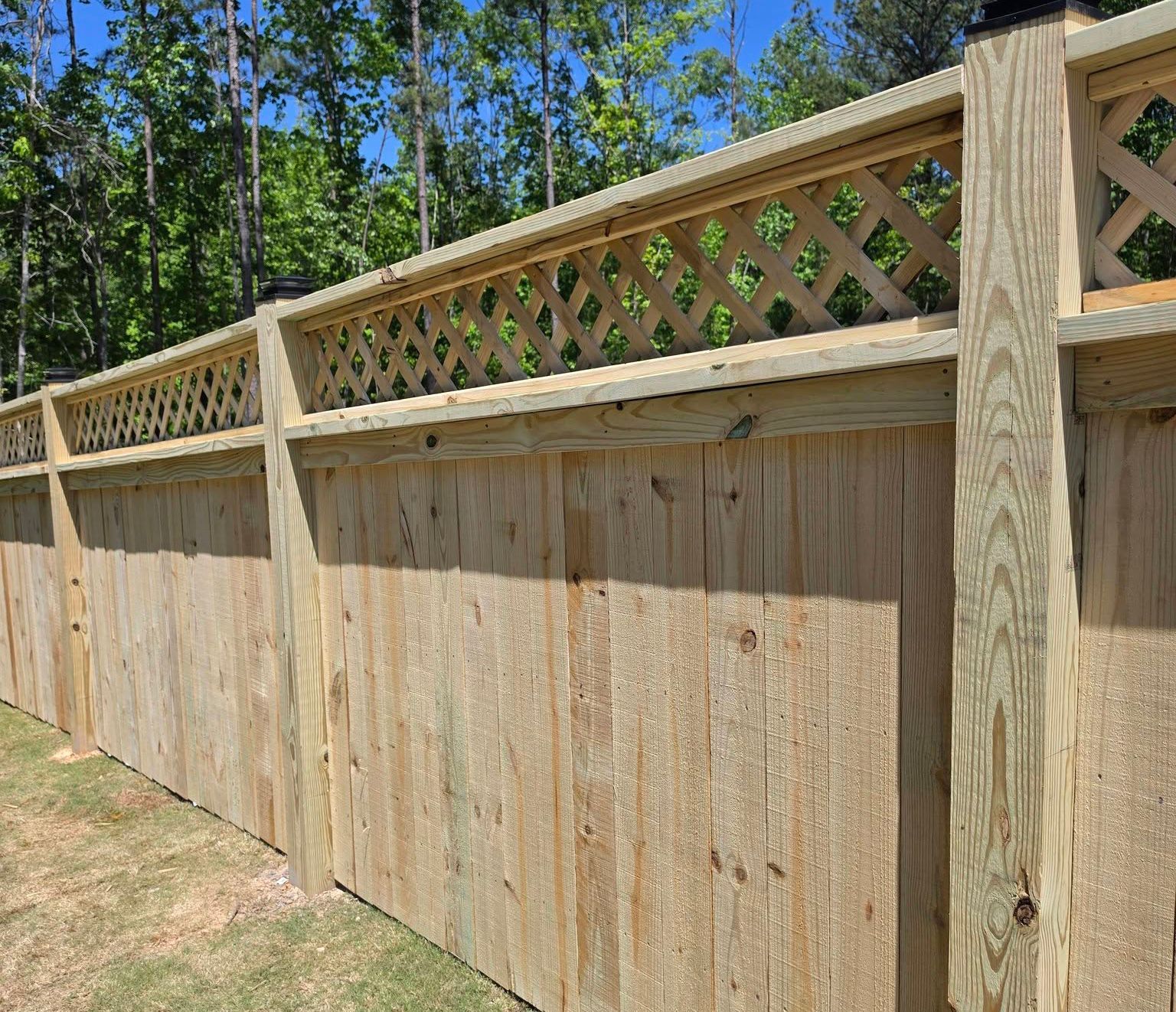 Wooden privacy fence with lattice top along a sunny, tree-lined yard