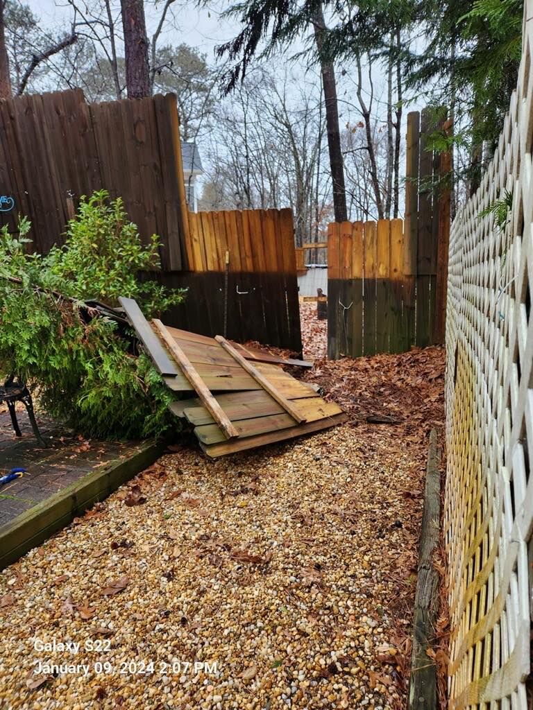 Backyard path with fallen wooden fence boards and gravel, beside a white lattice fence