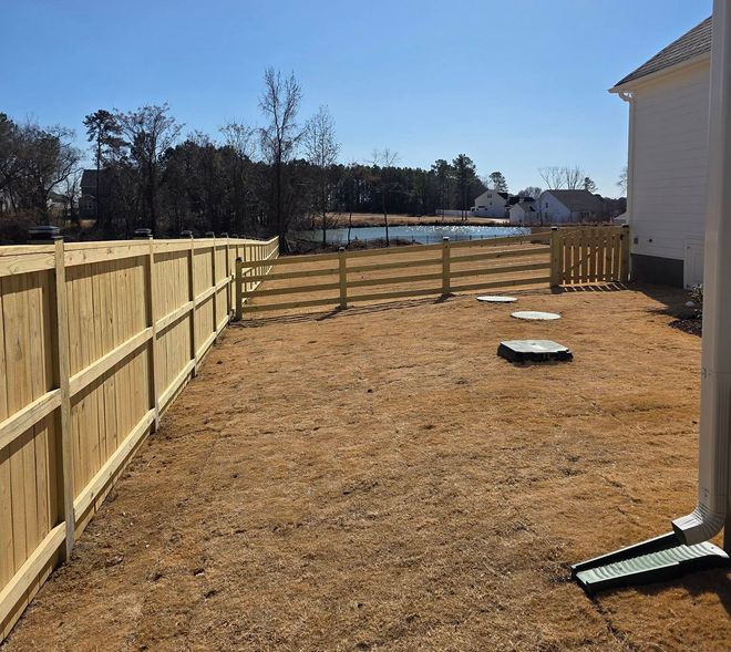 Fenced backyard with dry grass, stepping stones, and a house along the right side