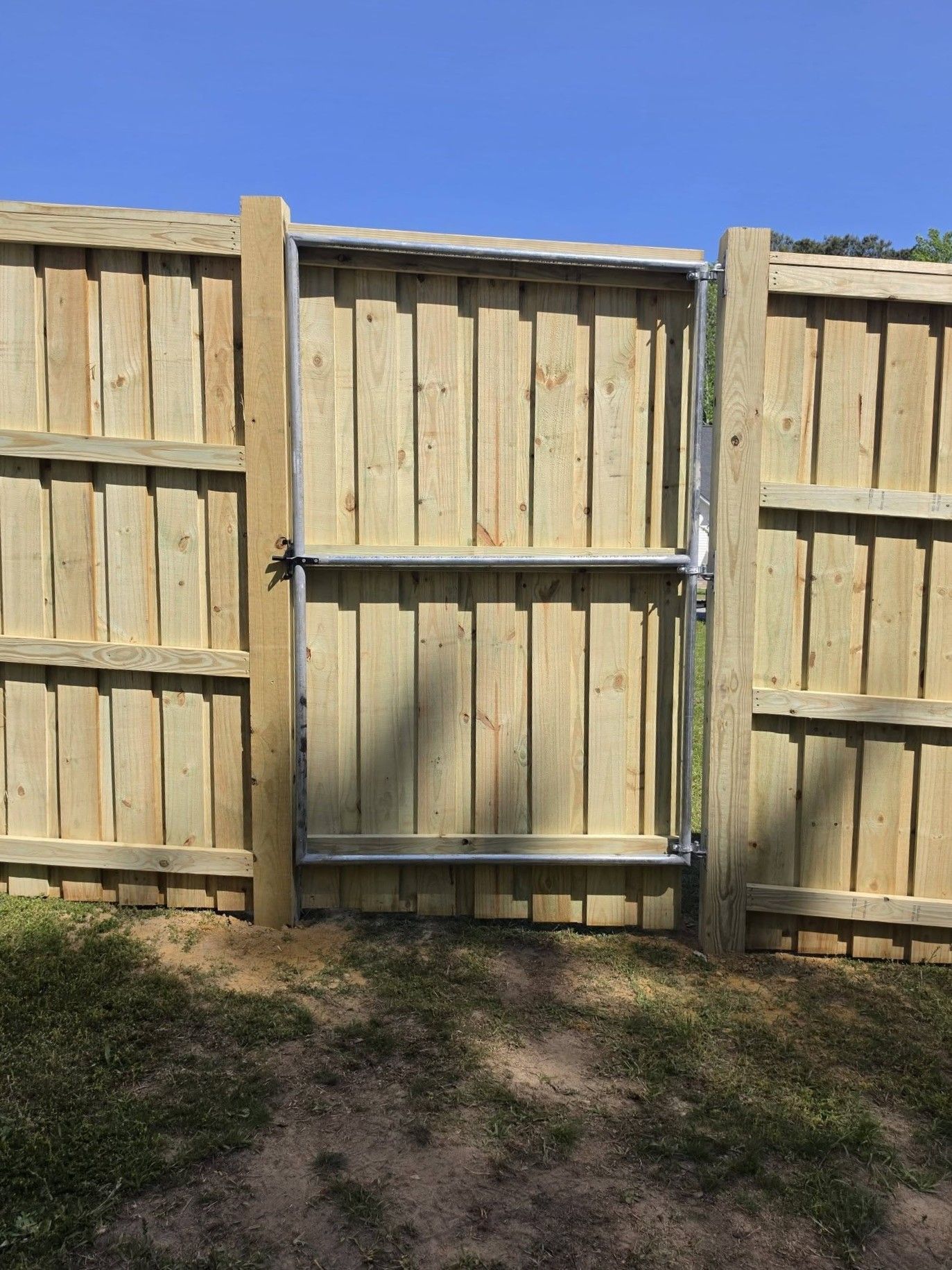 Wooden backyard fence with a closed gate and metal latch under a clear blue sky