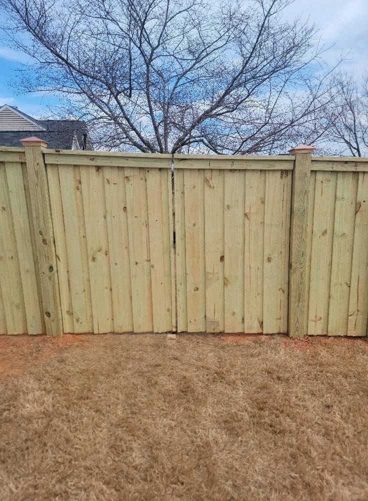 Wooden privacy fence in a dry backyard beneath a leafless tree and blue sky.
