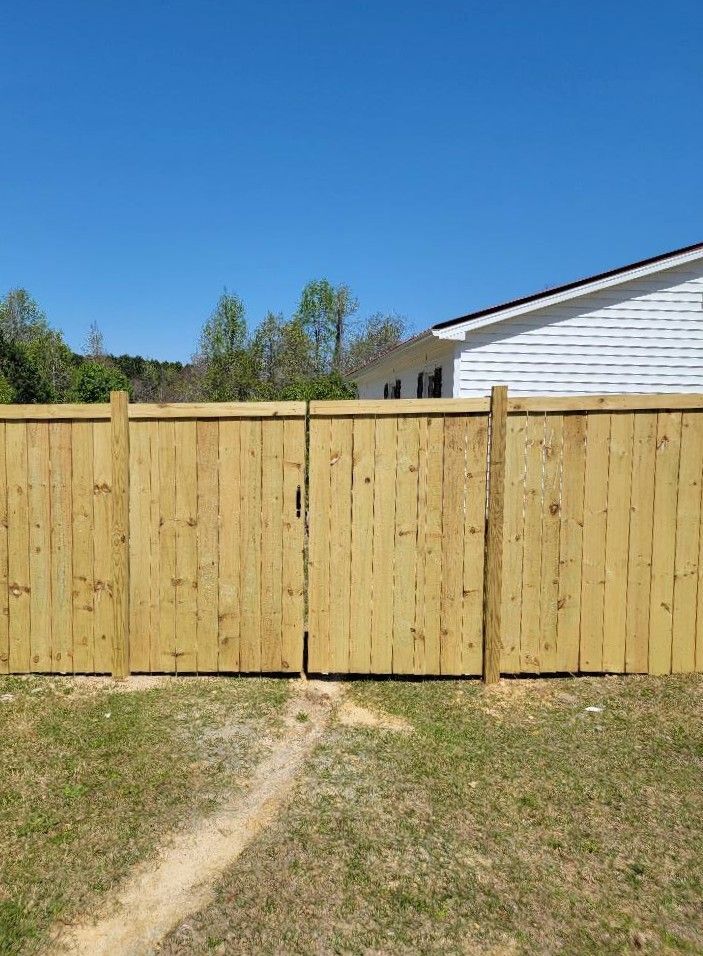 Wooden privacy fence with gate in a grassy backyard under a clear blue sky