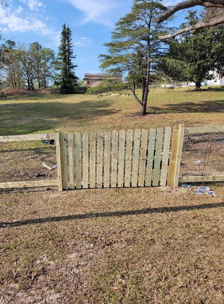 Weathered wooden fence panel blocking a grassy park path with trees in the background