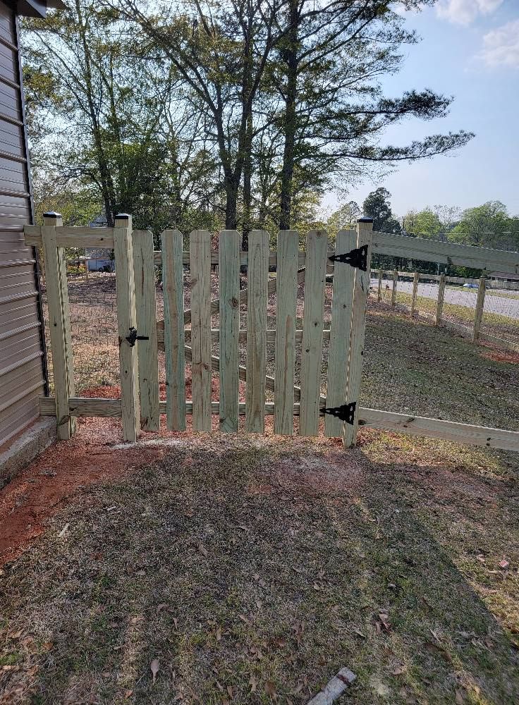 White wooden gate beside a house, opening to a yard with trees and a gravel path.