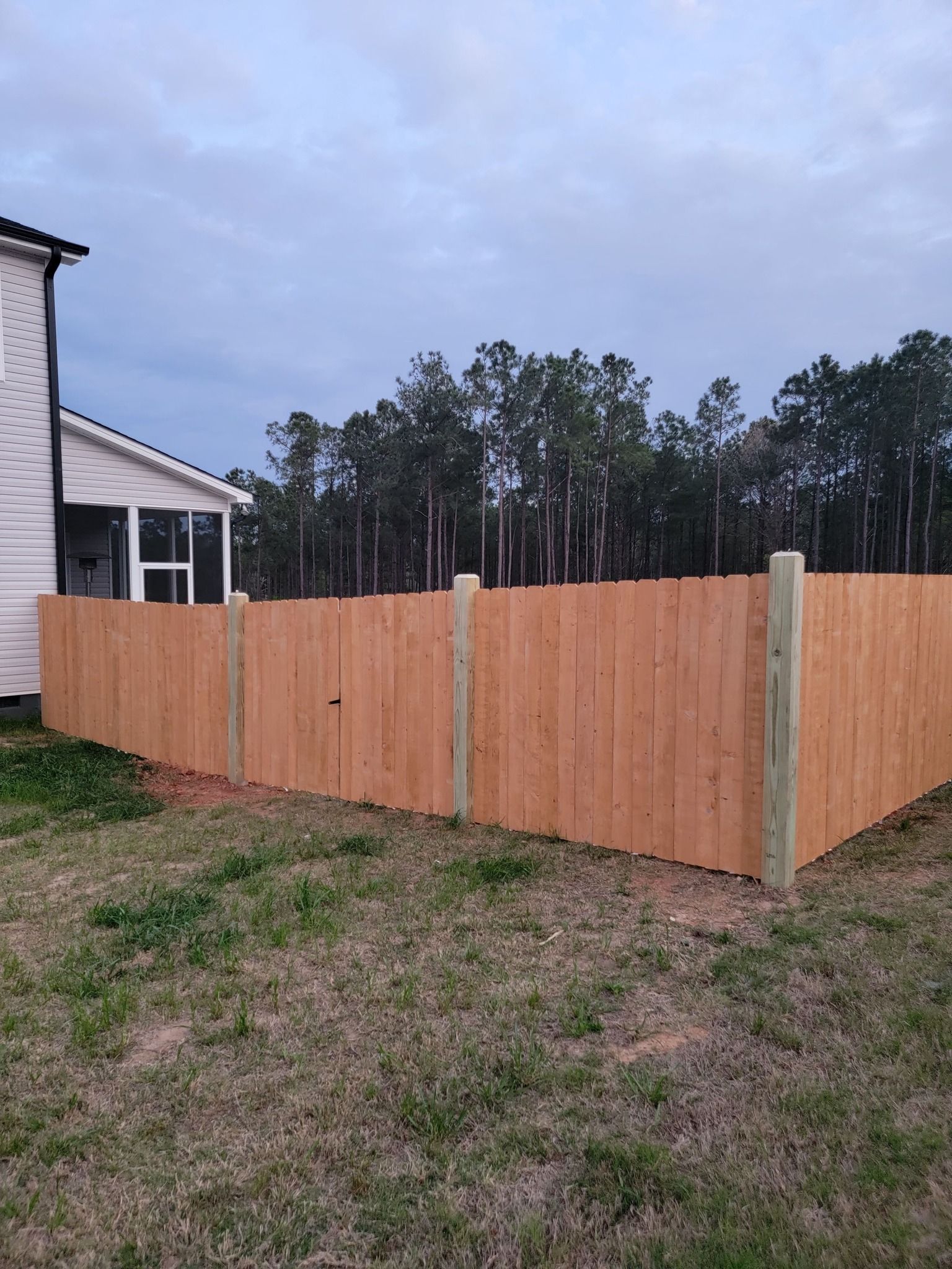 New wooden fence enclosing a backyard beside a house at dusk