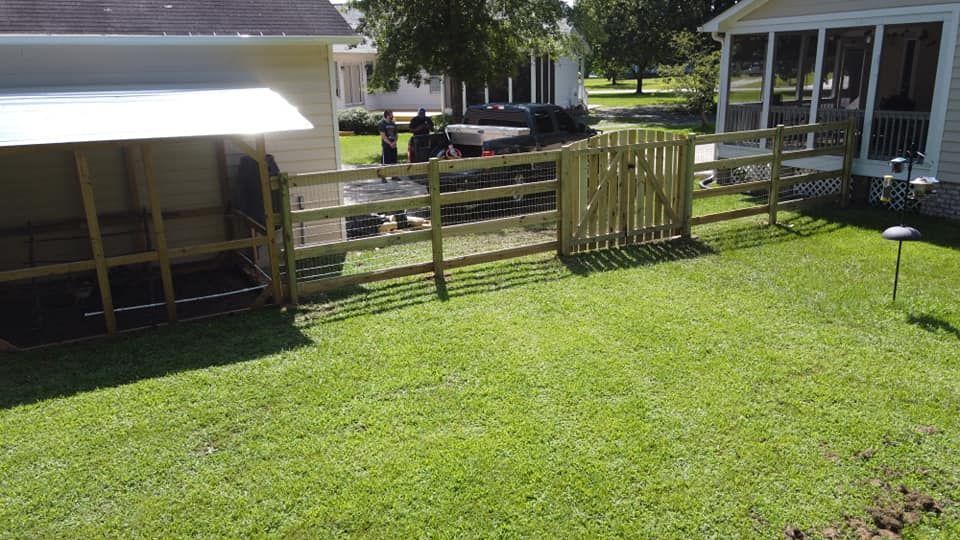 Backyard with green lawn, wooden fence gate, and small shed beside a house in bright sunlight