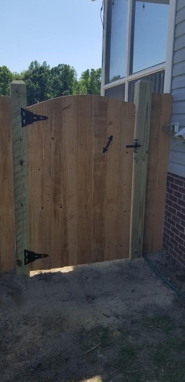 Open wooden gate beside a brick house, leading to a grassy yard under bright daylight