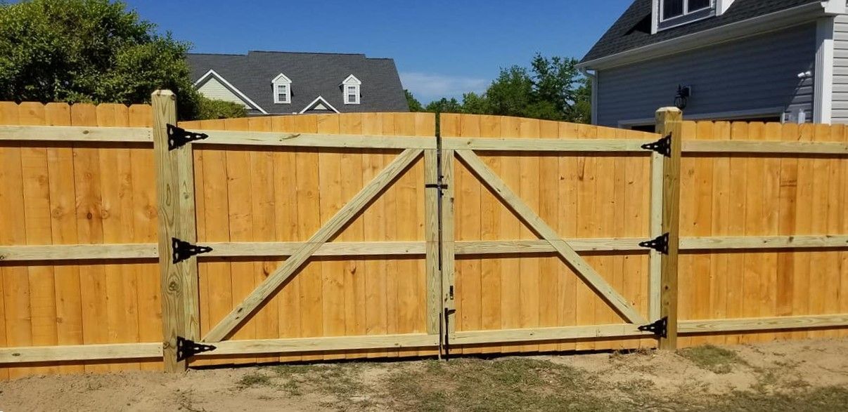 Wooden double driveway gate with metal braces in a fenced backyard, with houses visible behind.