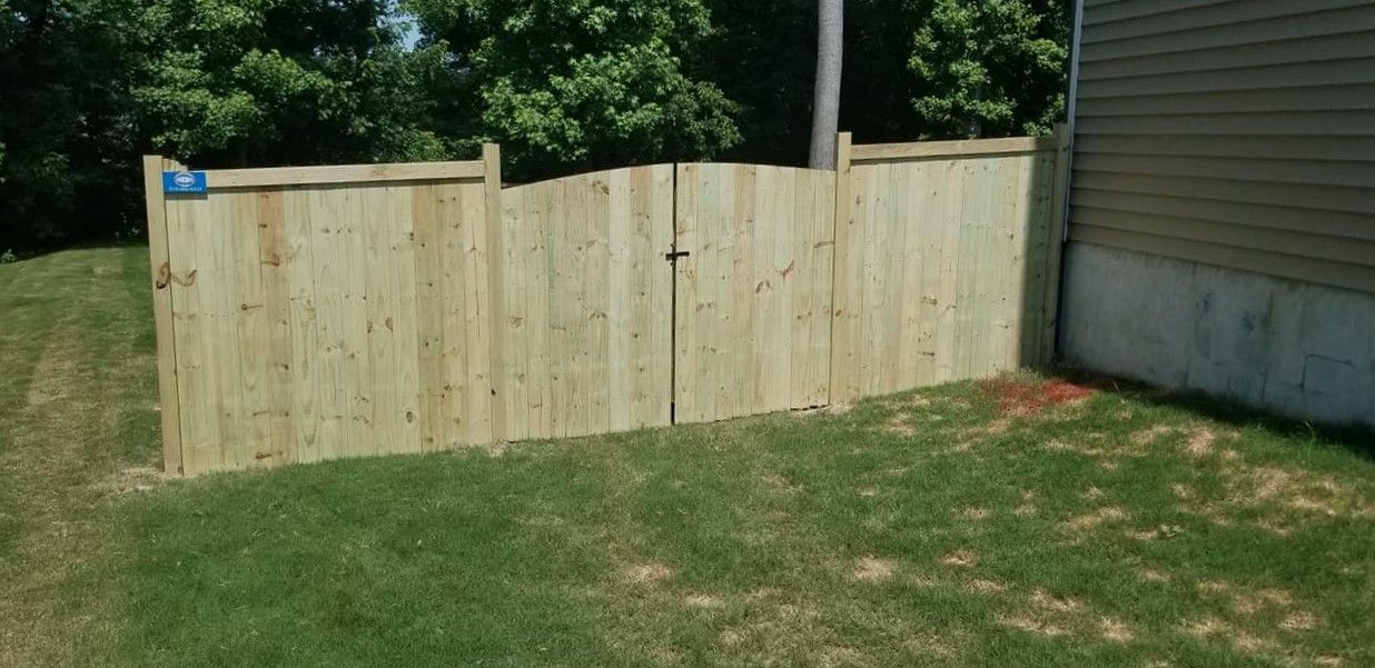 Wooden privacy fence panels across a grassy backyard beside a concrete wall and trees