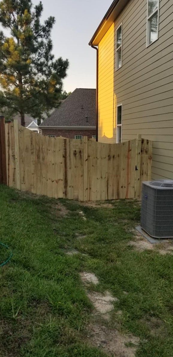 Narrow grassy side yard beside a house, with a wooden fence and an air conditioner unit.