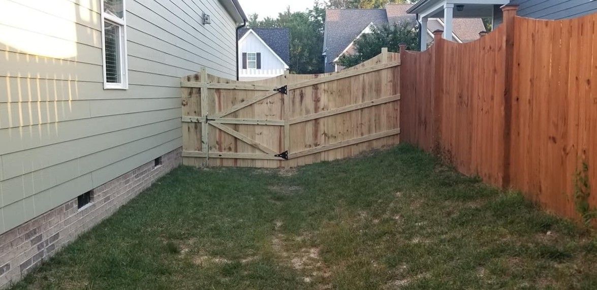 Narrow grassy backyard between a house and wooden fence, with a gate at the far end.