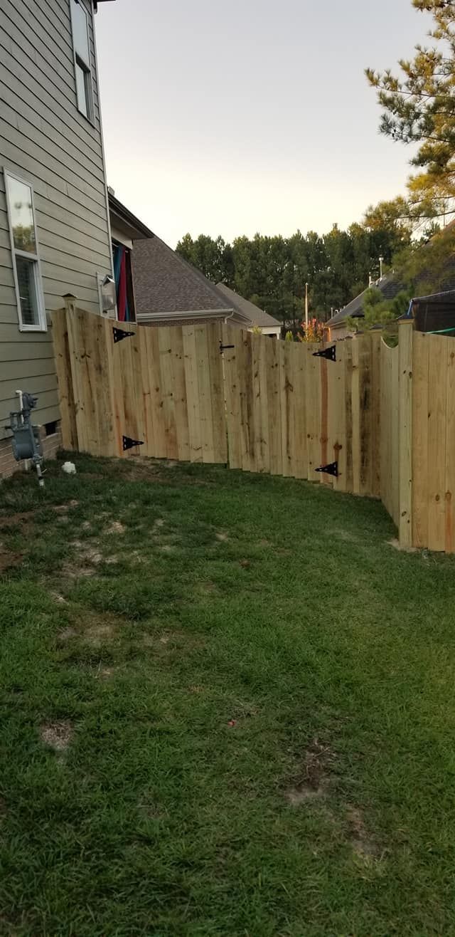 Backyard with fresh wooden fence panels beside a house and grassy lawn at dusk