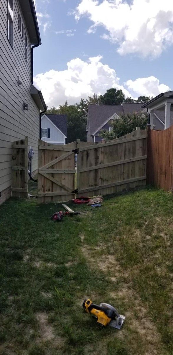 Backyard with wooden fence gate, grass, and a yellow-black power tool on the ground.