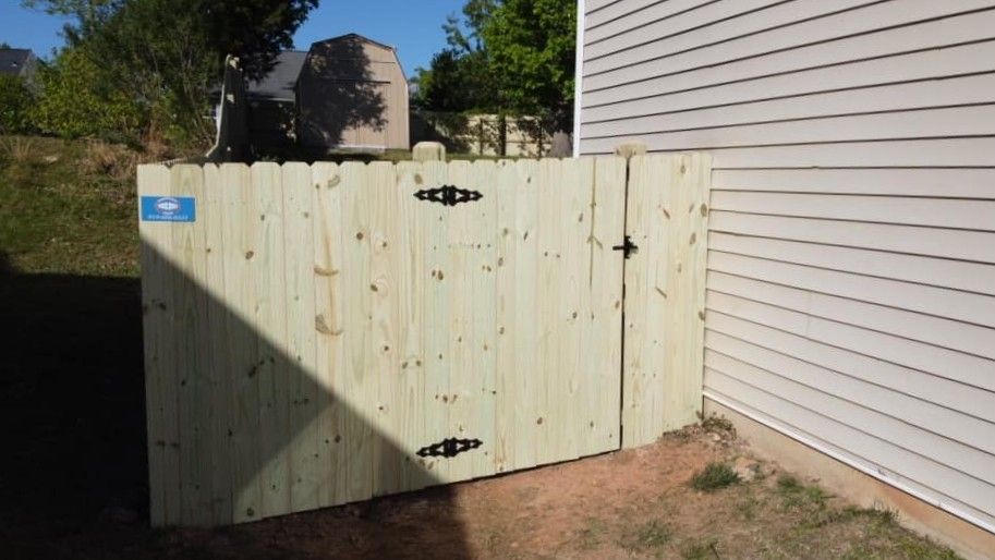 Pale green wooden gate beside a white house, partly in shadow, in a backyard.