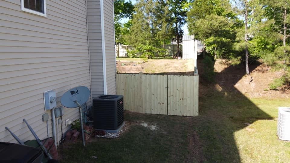 Backyard beside a house with HVAC unit, fence, trees, and a grassy slope