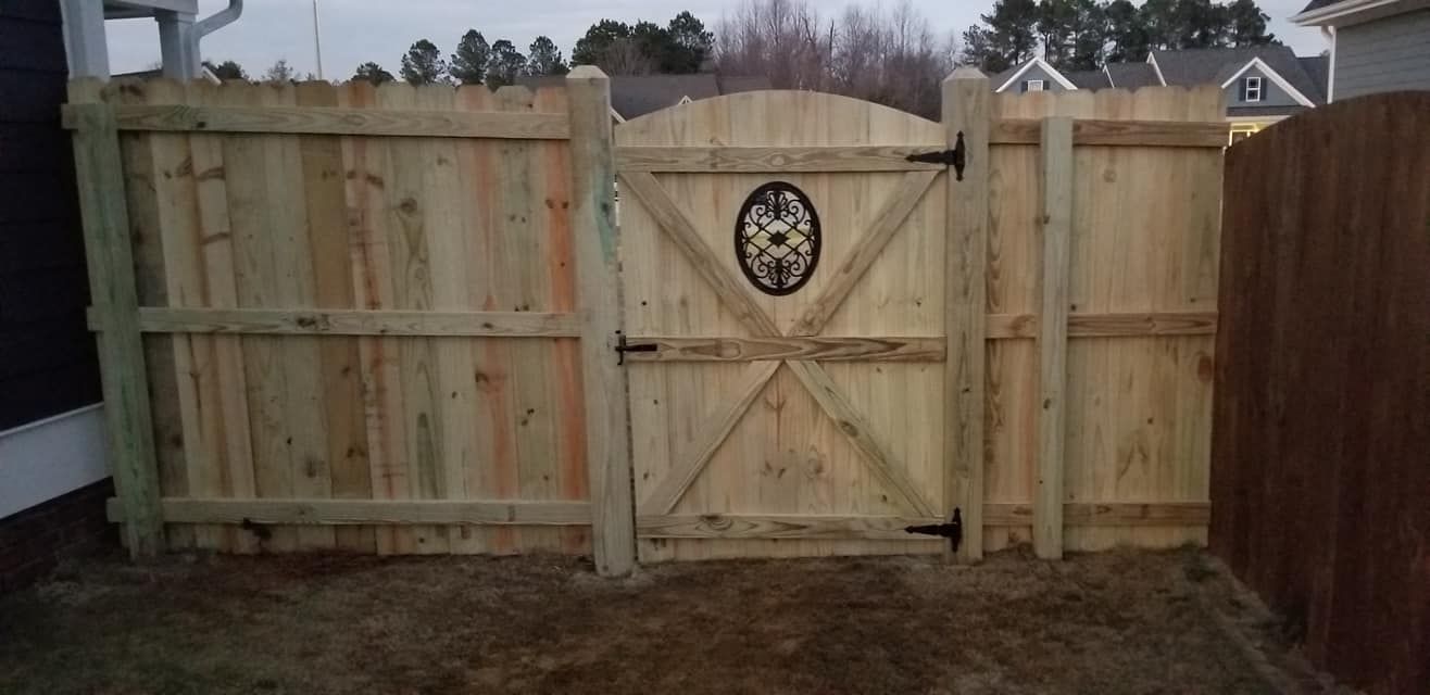 Wooden backyard fence with a central gate and oval decorative emblem at dusk