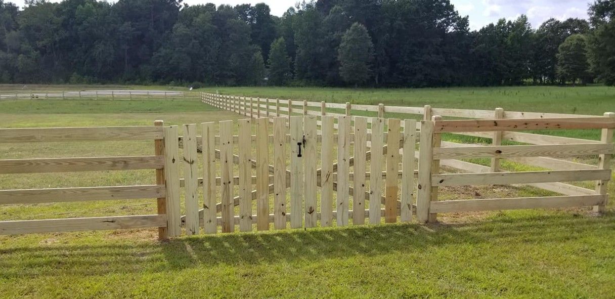 Wooden gate and fence in a grassy field with trees in the background